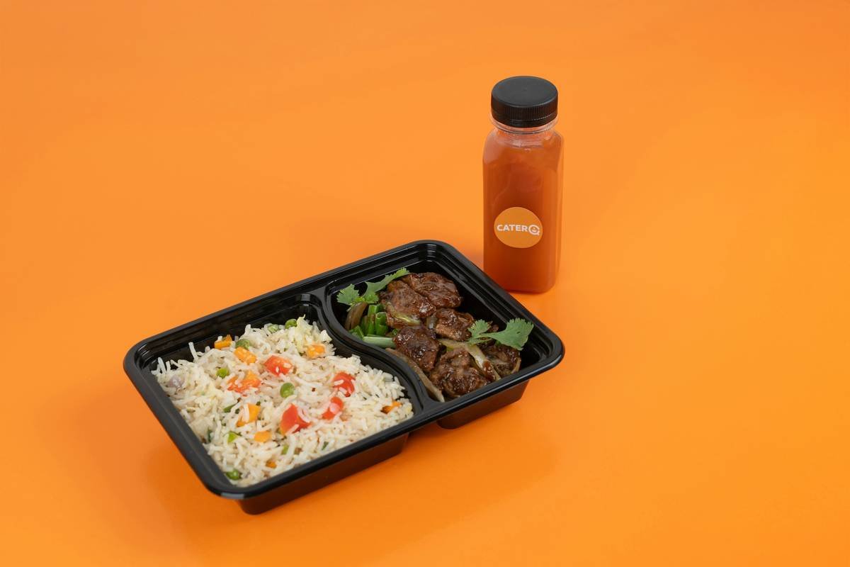 A plastic container of food next to a bottle of sauce