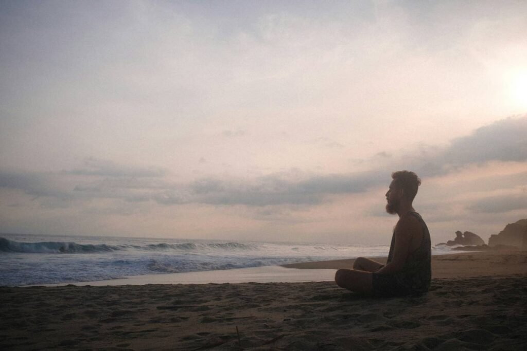 guy sits cross-legged on the beach and meditates, the wide sea in the background